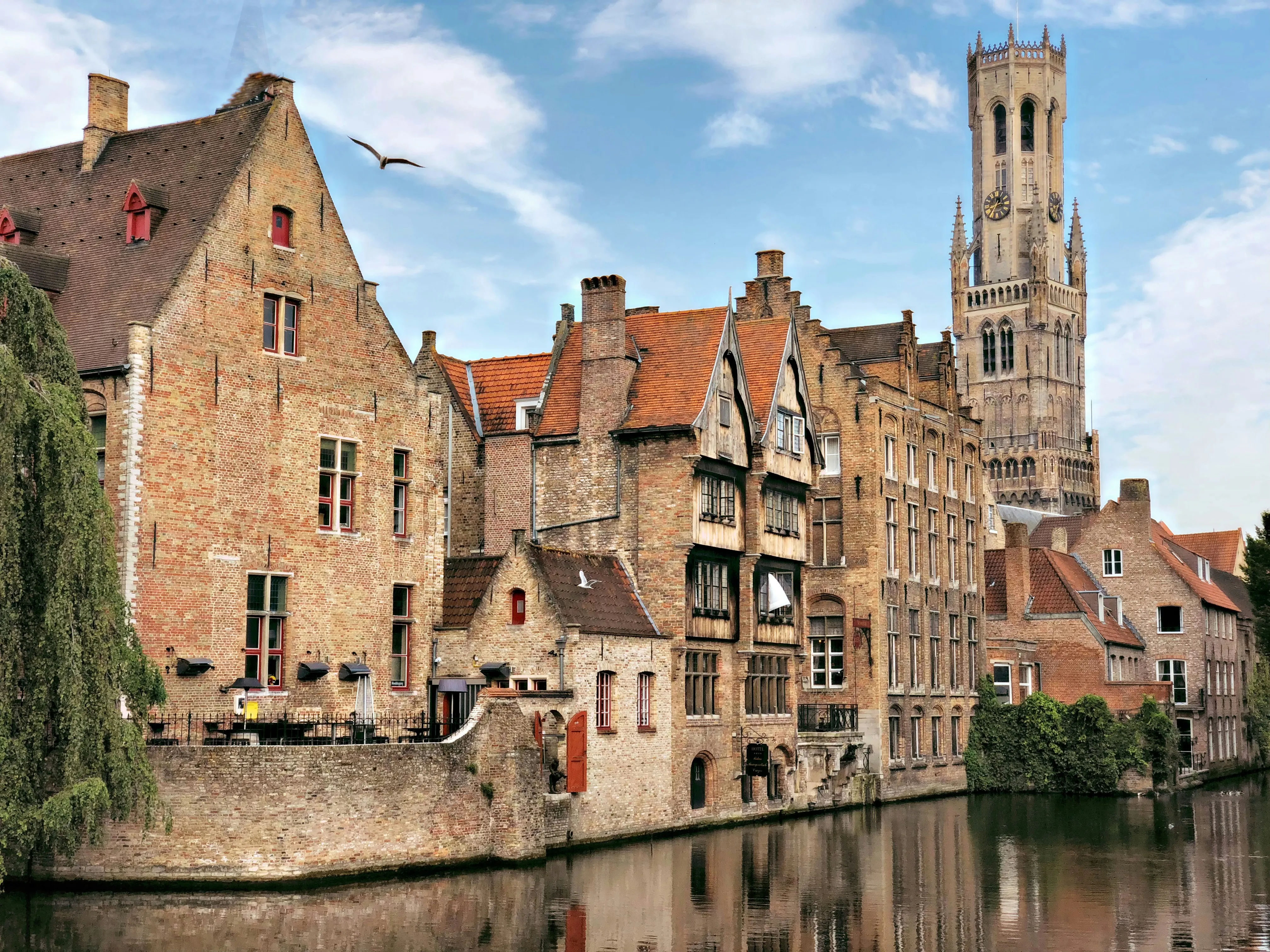 Les façades flamandes en briques et le beffroi se reflétant dans l'eau d'un canal à Bruges