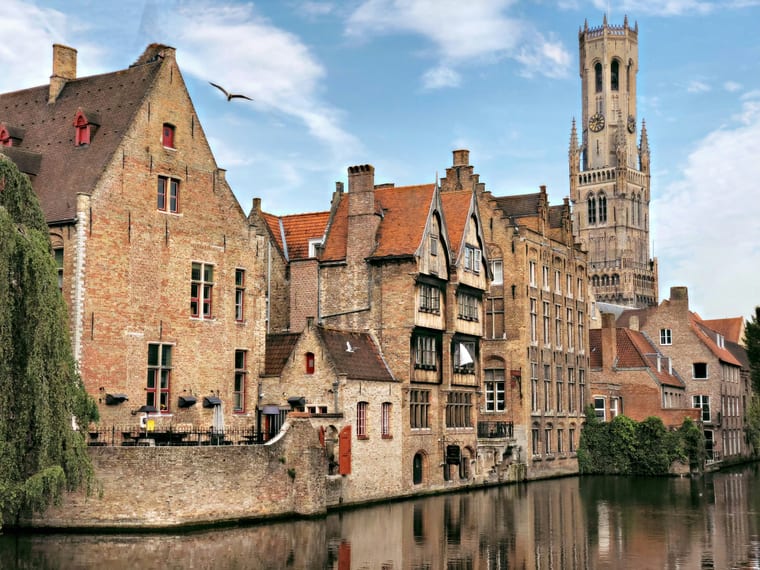 Les façades flamandes en briques et le beffroi se reflétant dans l'eau d'un canal à Bruges