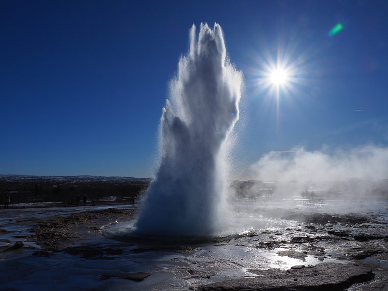 Le geyser Strokkur en éruption avec des visiteurs en arrière-plan