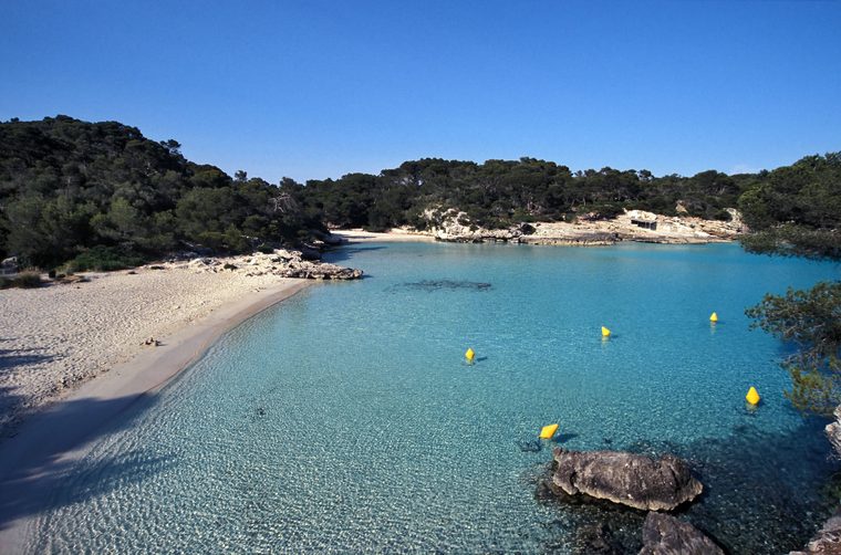 Les eaux turquoise d'une crique du sud de Minorque, entourée de falaises calcaires et de pins