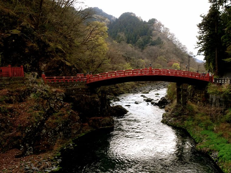 Le pont sacré Shinkyo rouge traversant la rivière entouré par la forêt à Nikko